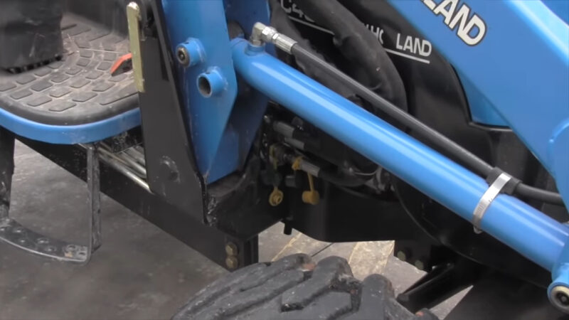 Close-up of a New Holland tractor’s hydraulic system, showing blue hydraulic pipes and mechanical components