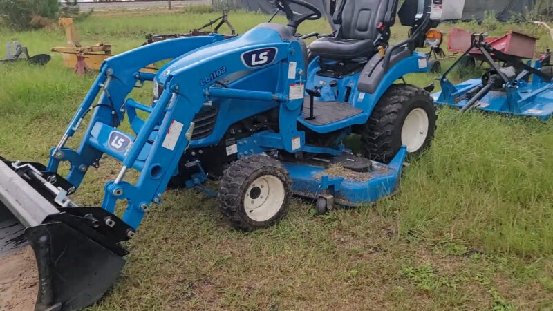 LS MT125 compact blue tractor with a front loader attachment, parked on a grassy field