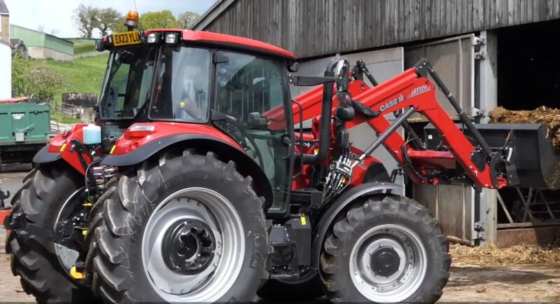 red Case IH Farmall tractor equipped with a front loader, parked near a barn on a farm