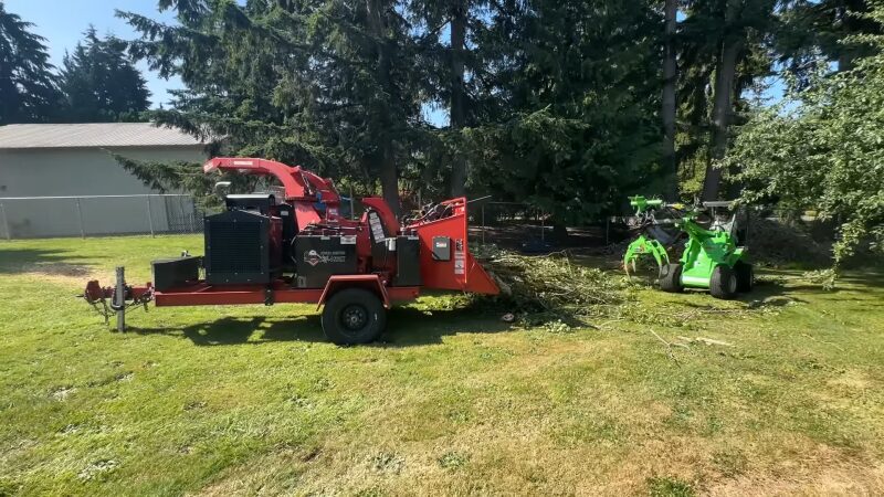 A Red Wood Chipper Processes Branches and Debris on A Grassy Area